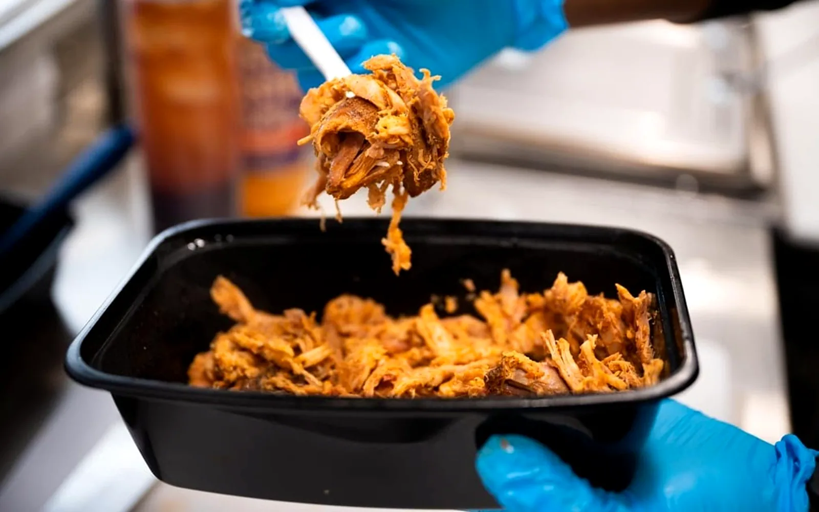 Fresh pulled pork being portioned into a takeout container